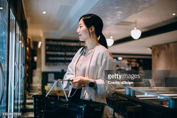 young asian woman carrying a shopping basket, grocery shopping for daily necessities in supermarket. healthy eating and home cooking lifestyle - shopping basket bildbanksfoton och bilder