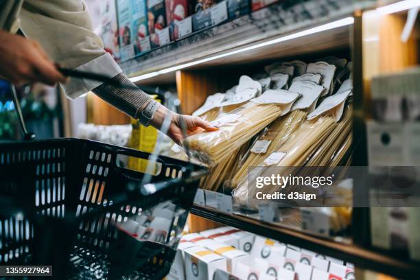 close up of young asian woman grocery shopping for daily necessities in supermarket, choosing a pack of organic italian pasta. healthy eating and home cooking lifestyle - bioladen stock-fotos und bilder