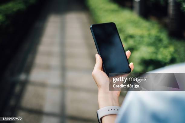 over the shoulder view of woman using smartphone while having a morning walk in park on a sunny morning. lifestyle and technology. smartphone with blank screen for design mockup - man walking phone stock-fotos und bilder