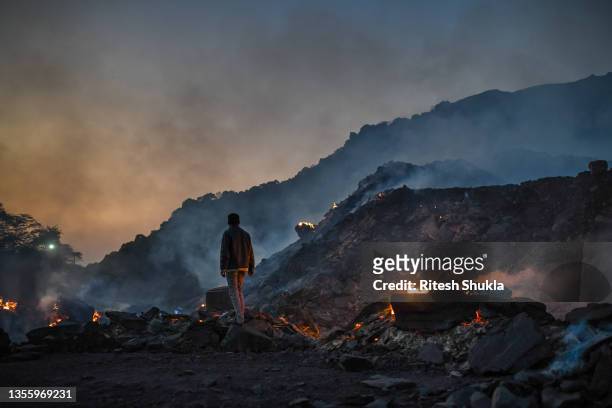 Man stands near burning coal waste inside a coal mine on November 22, 2021 in Sonbhadra, Uttar Pradesh, India. India is rapidly transitioning to...