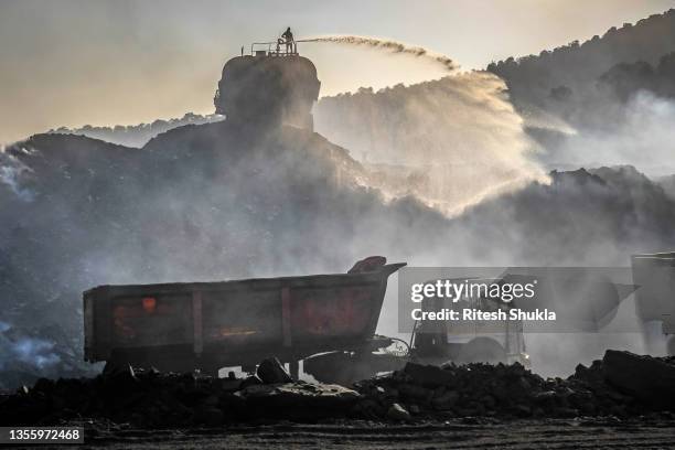 Worker sprays water to help settle pollution caused by truck and coal-loading activity at a coal mine on November 23, 2021 in Sonbhadra, Uttar...