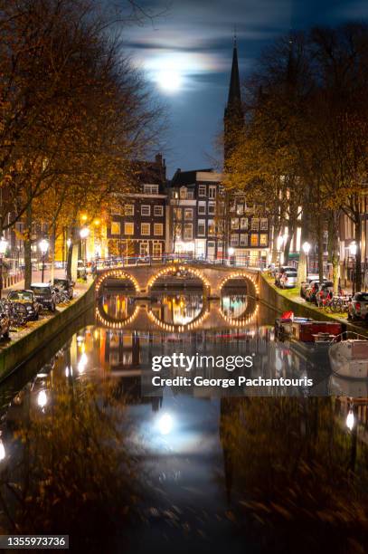 full moon and a calm canal in amsterdam, holland at night - amsterdam dusk evening foto e immagini stock