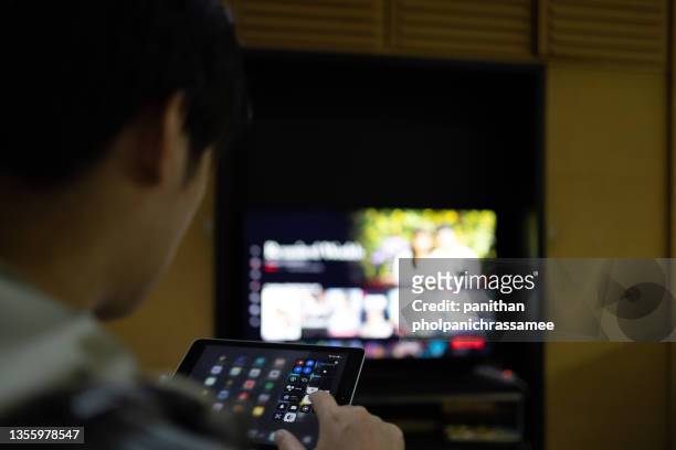close up asian man control televistion with mobile device. - tv phone tablet stock-fotos und bilder