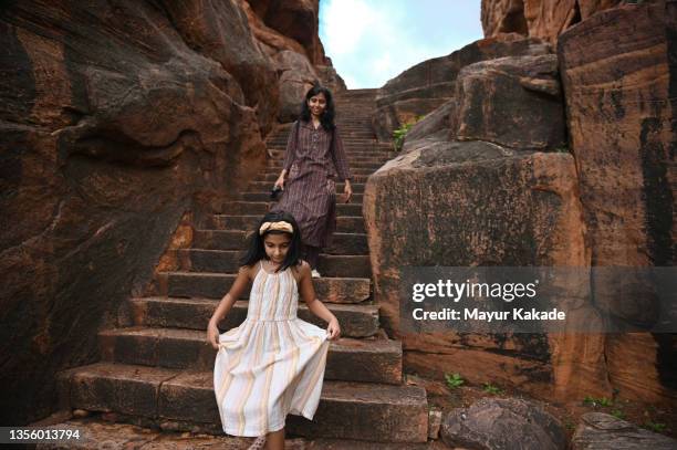 mother and daughter climbing down steps of an ancient hindu stone cave temple, badami, karnataka - asian family fall stock-fotos und bilder