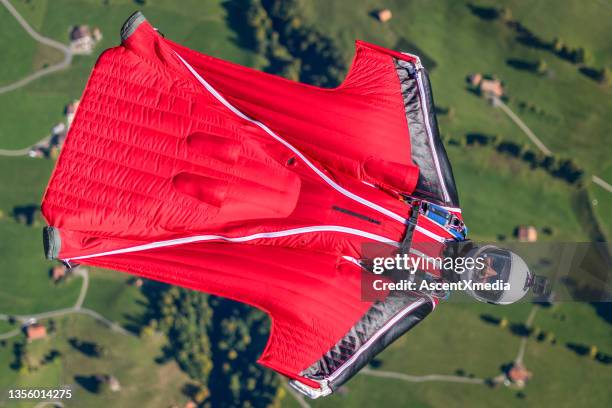 man in wingsuit glides, upside down, over scene - wing suit stock pictures, royalty-free photos & images