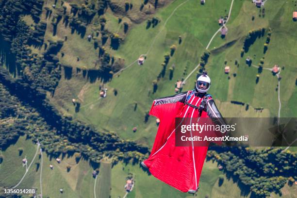 man in wingsuit glides, upside down, over scene - base jumping stock pictures, royalty-free photos & images