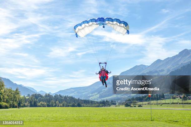 paraglider kommt herein, um auf grasbewachsener wiese zu landen - landung stock-fotos und bilder