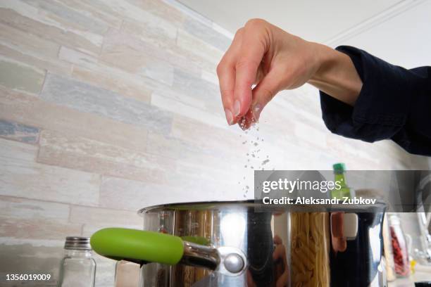 cooking italian pasta with cream sauce and basil, at home. a girl or woman cooks and stirs penne pasta in a pot. vegetarian food. step-by-step instructions, do it yourself. step 4. - sales occupation fotografías e imágenes de stock