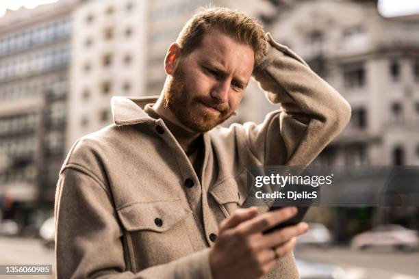 disappointed man using phone on city street. - autumn sadness stock pictures, royalty-free photos & images