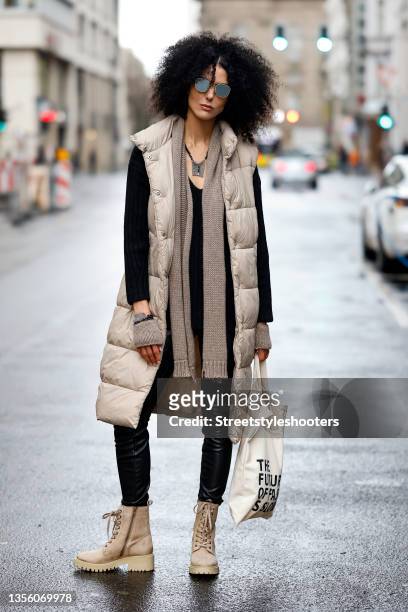 Model Zoe Helali wearing a long beige puffer vest by Guido Maria Kretschmer - About You, a black knitted v-neck pullover by Guido Maria Kretschmer -...