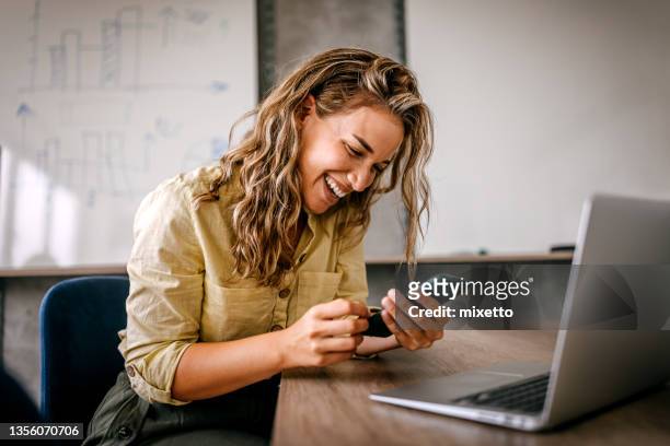 women using smartphone and laptop laughing - cool office stockfoto's en -beelden