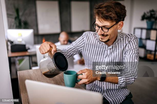geschäftsmann gießt kaffee am arbeitsplatz ein - kaffeemaschine stock-fotos und bilder