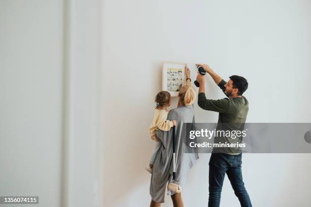 family hanging a painting on the wall - photo wall stock pictures, royalty-free photos & images