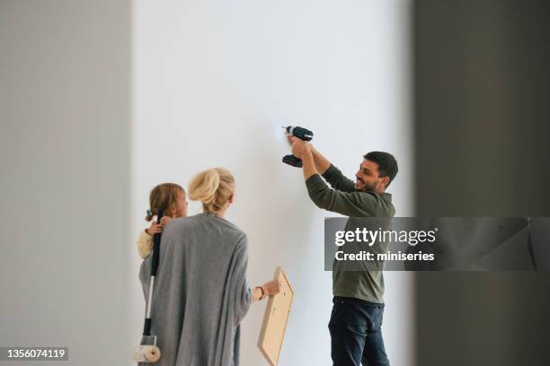 family hanging a painting on the wall - drill stockfoto's en -beelden