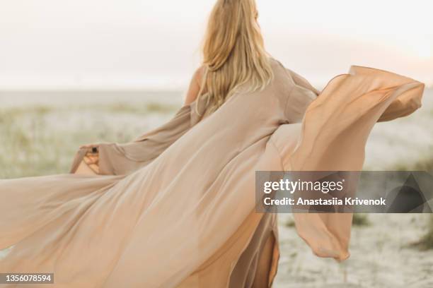 woman wearing beige silk developing dress against the seaside. - beach vibes stock-fotos und bilder