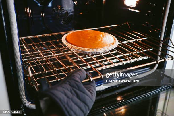 woman removes pumpkin pie from oven - a fall from grace - fotografias e filmes do acervo
