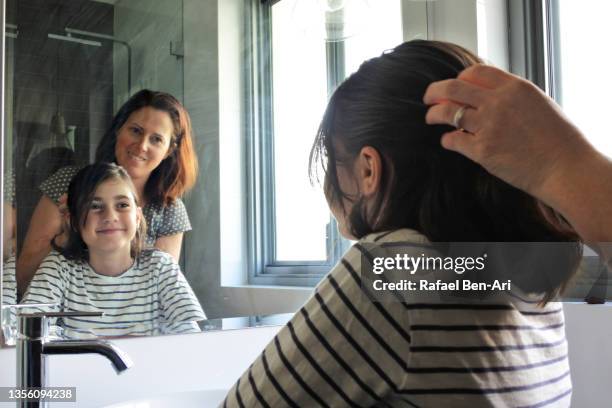 mother combing her daughter hair in home bathroom - man combing hair stock-fotos und bilder