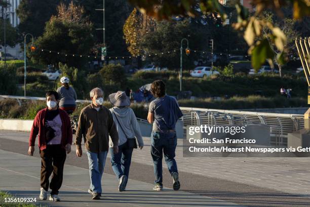 Masked walkers stroll near Lake Merritt in Oakland, Calif. On Sunday, Nov. 28, 2021. The discovery of the Omicron variant comes at a delicate time...