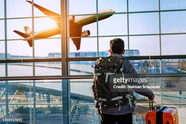 male tourist is standing in airport and looking at aircraft flight through window. - airport bildbanksfoton och bilder