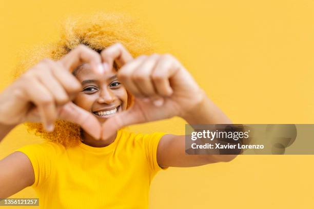 portrait of cheerful african american woman making a hand-drawn heart shape over yellow background - hand drawn love heart stock-fotos und bilder