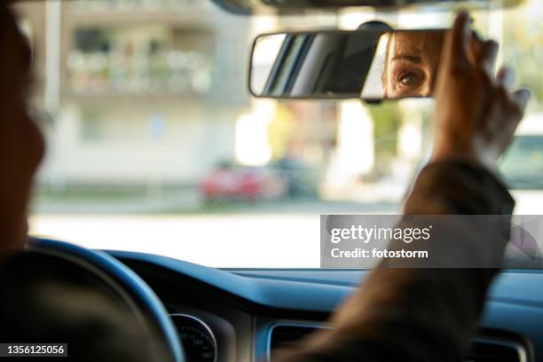 mature woman sitting in her car and adjusting rear view mirror - rear view mirror eyes stock pictures, royalty-free photos & images