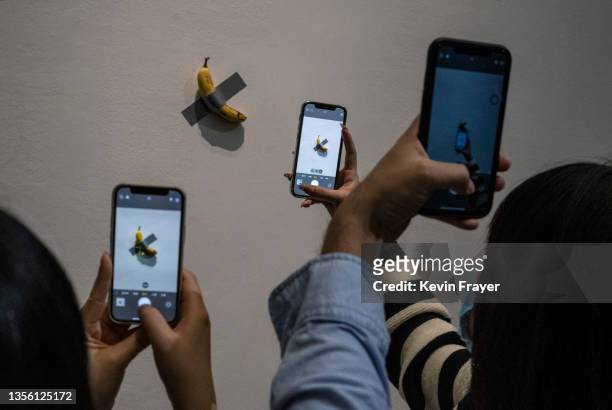Visitors take pictures of the work "Comedian" by Italian artist Maurizio Cattelan that is part of his exhibition "The Last Judgement'' at the UCCA...