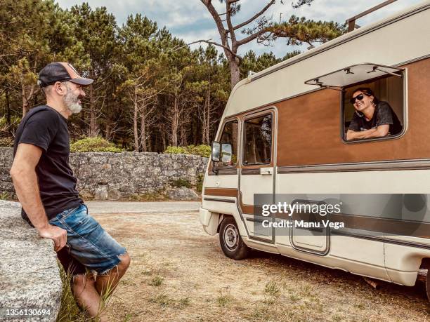 a woman inside a motorhome leaning out of a window looking out at her partner who is outside watching her happily. - camping indoors stock pictures, royalty-free photos & images