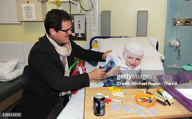 In this handout image provided by the FA, Manager Fabio Capello of England helps patient Tiarnan Smith into a football shirt during a visit to Great...