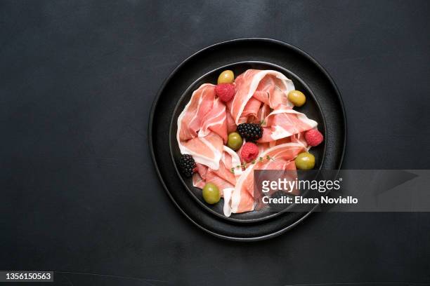 parma ham italian pork prosciutto  with olives on a black dish. traditional antipasto appetizer for dinner or lunch in restaurant. - charcuterie stock-fotos und bilder