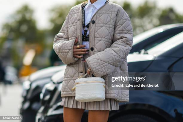 Camila Coelho wears a white shirt, a black shiny leather with embroidered pearls strappy t-shirt, a beige quilted puffer jacket from Dior, a white...