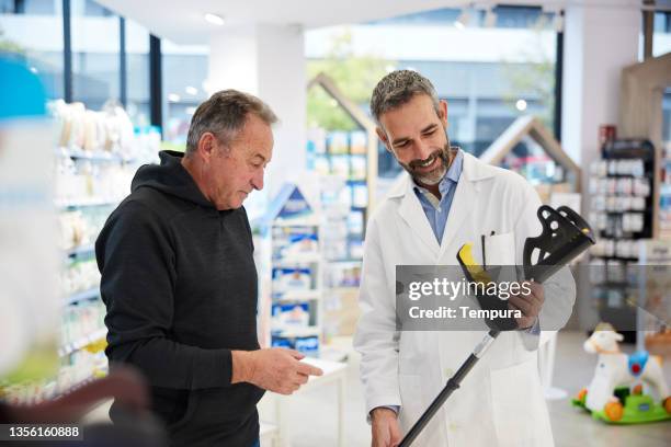 ein apotheker zeigt einem älteren kunden eine krücke. - medizinisches-material stock-fotos und bilder