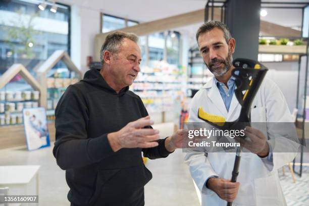 a pharmacist shows a crutch to a client. - crutches stockfoto's en -beelden