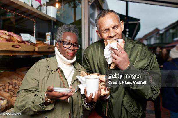 senior man eating doughnut standing by female friend - donut man bildbanksfoton och bilder