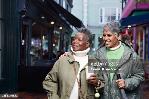 senior women looking away in market - white and black women and umbrella stockfoto's en -beelden