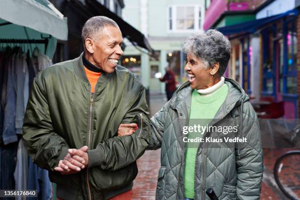 senior couple standing on street in market - arm in arm stockfoto's en -beelden