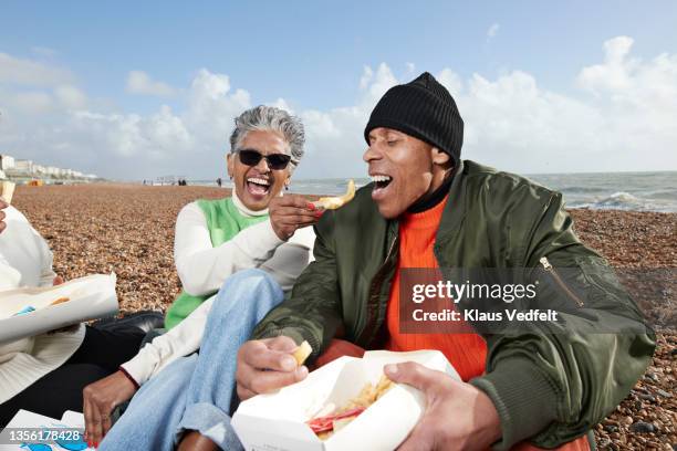 cheerful senior woman feeding fish to man at beach - couple de vieux drole photos et images de collection