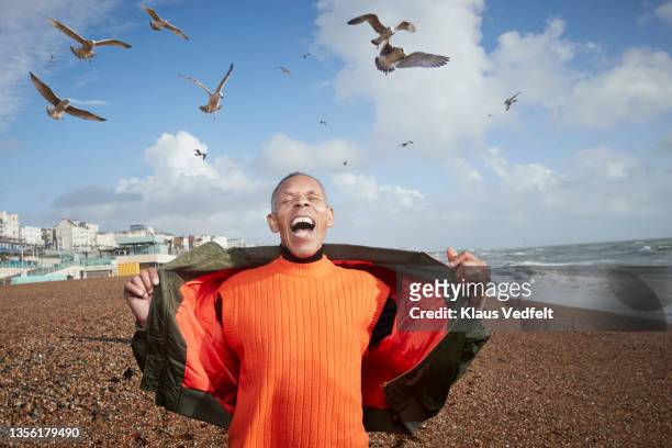 senior man screaming while birds flying at beach - jacket fotografías e imágenes de stock