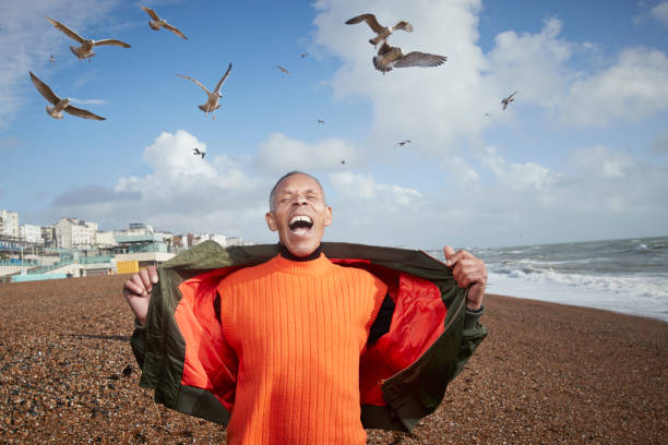 senior man screaming while birds flying at beach - homme joyeux photos et images de collection