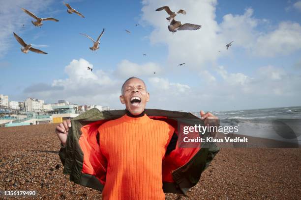 senior man screaming while birds flying at beach - libero foto e immagini stock