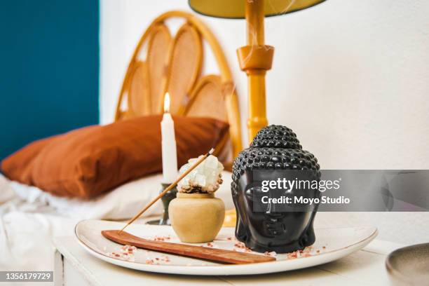 shot of a buddha ornament, incense stick and candle in an empty bedroom during the day - wierook stockfoto's en -beelden