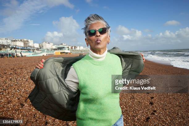 senior woman puckering at beach during vacation - gray coat stock pictures, royalty-free photos & images