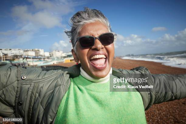 cheerful senior woman screaming at beach - freedom of expression stock-fotos und bilder