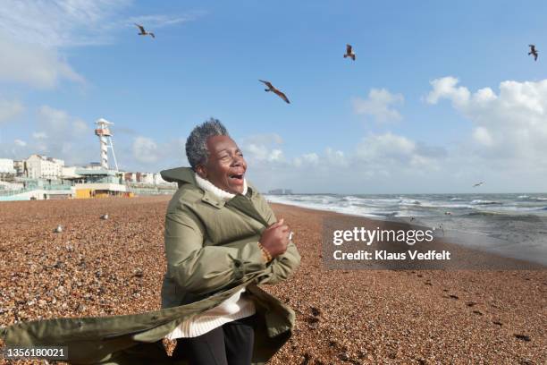 senior woman holding jacket while standing in wind - four day old stock pictures, royalty-free photos & images