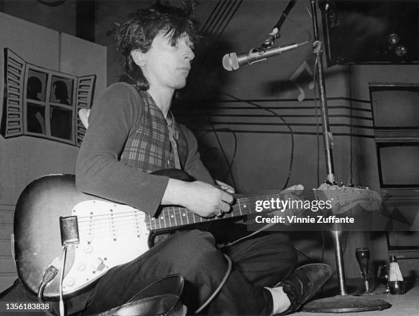 American guitarist, singer and songwriter Johnny Thunders sitting cross legged as he performs an impromptu gig at the Limelight in New York City, New...