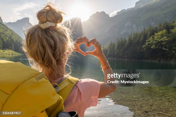 wanderfrau macht einen herzförmigen fingerrahmen auf der spektakulären alpenlandschaft, um liebe zum umweltkonzept zu zeigen - journey stock-fotos und bilder