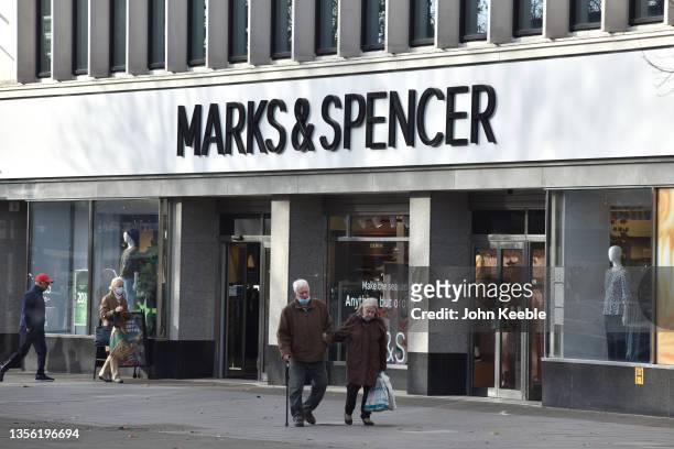 An elderly couple wearing face masks walk past a Marks and Spencer store on the High Street on November 29, 2021 in Brentwood, England. Six cases of...