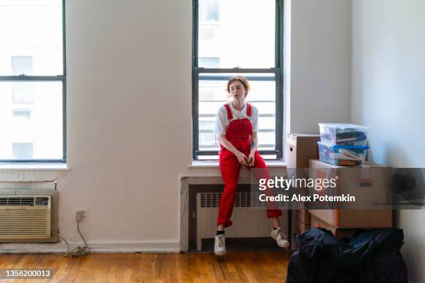 relocation to a new apartment. young woman is sitting on a windowsill in an empty room of a newly rented apartment, tired after moving in. - apartments rent stock pictures, royalty-free photos & images