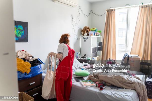 young slender woman is packing her stuff preparing to move to a new apartment - messy bedroom 個照片及圖片檔