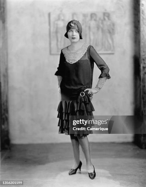 Young woman in a 'flapper' dress and cloche hat posing for portrait with hands on hips. Circa 1922