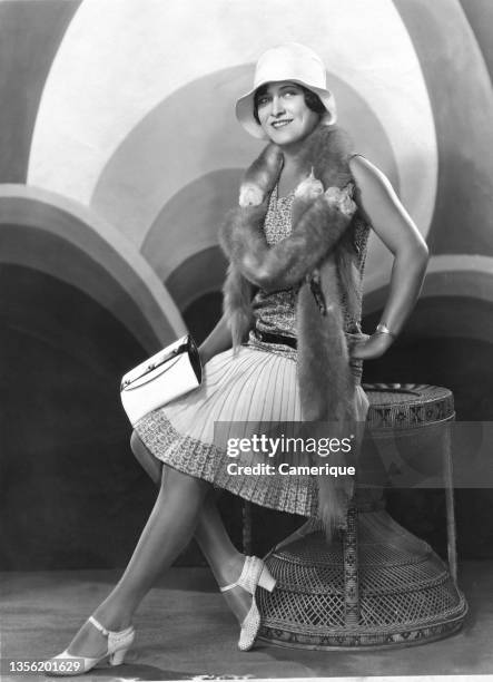 Young woman, a model in 1920's outfit with pleated dress, white shoes, fur wrap, white hat and white pocketbook.